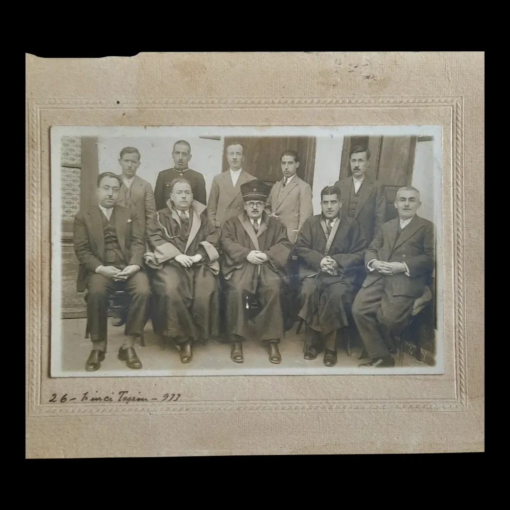 Card-mounted photograph of a court panel with three robed figures seated in the front row, and a handwritten date below