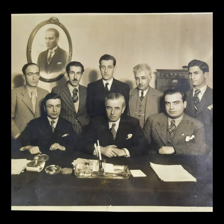 Group of eight posing at a desk in an office with a portrait of Atatürk on the wall