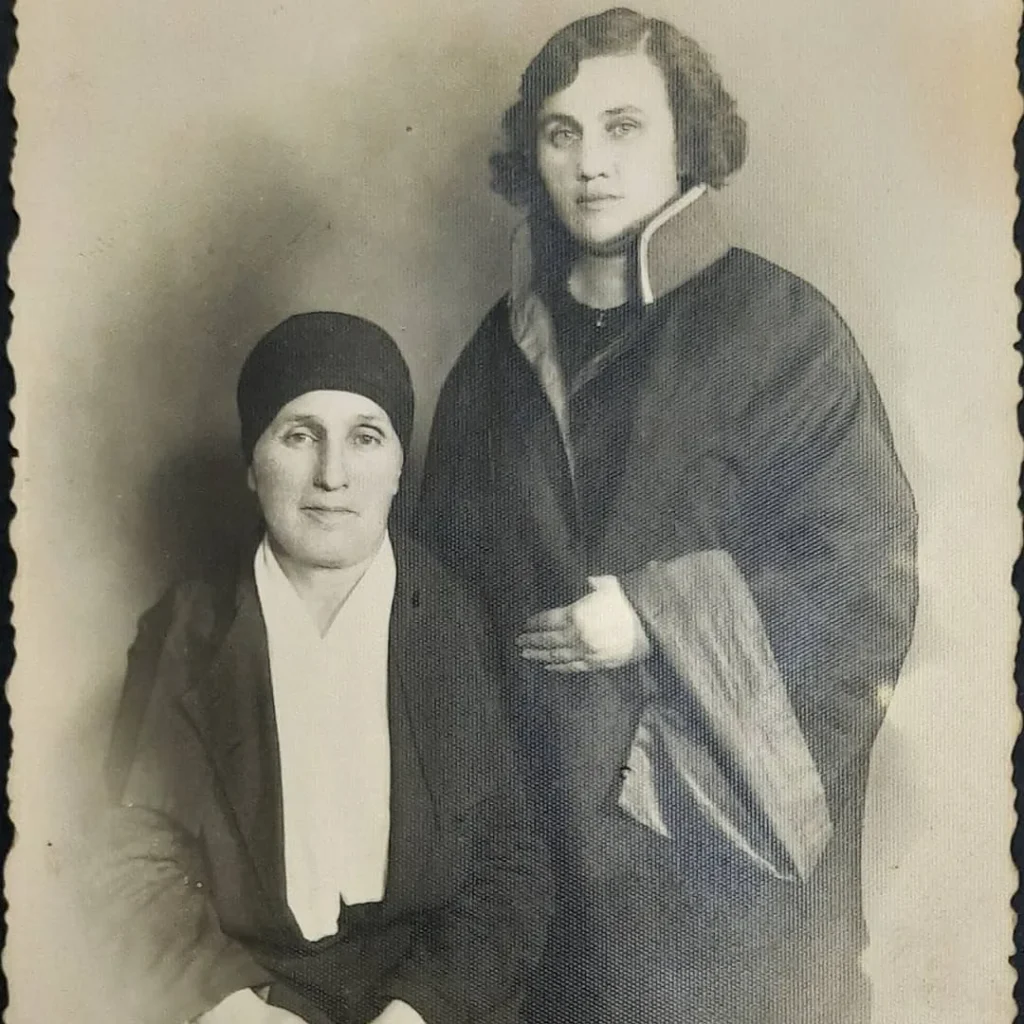 Oturan başı örtülü yaşlı kadın ve yanında ayakta duran, geniş yakalı koyu giysili genç kadının stüdyo portresi