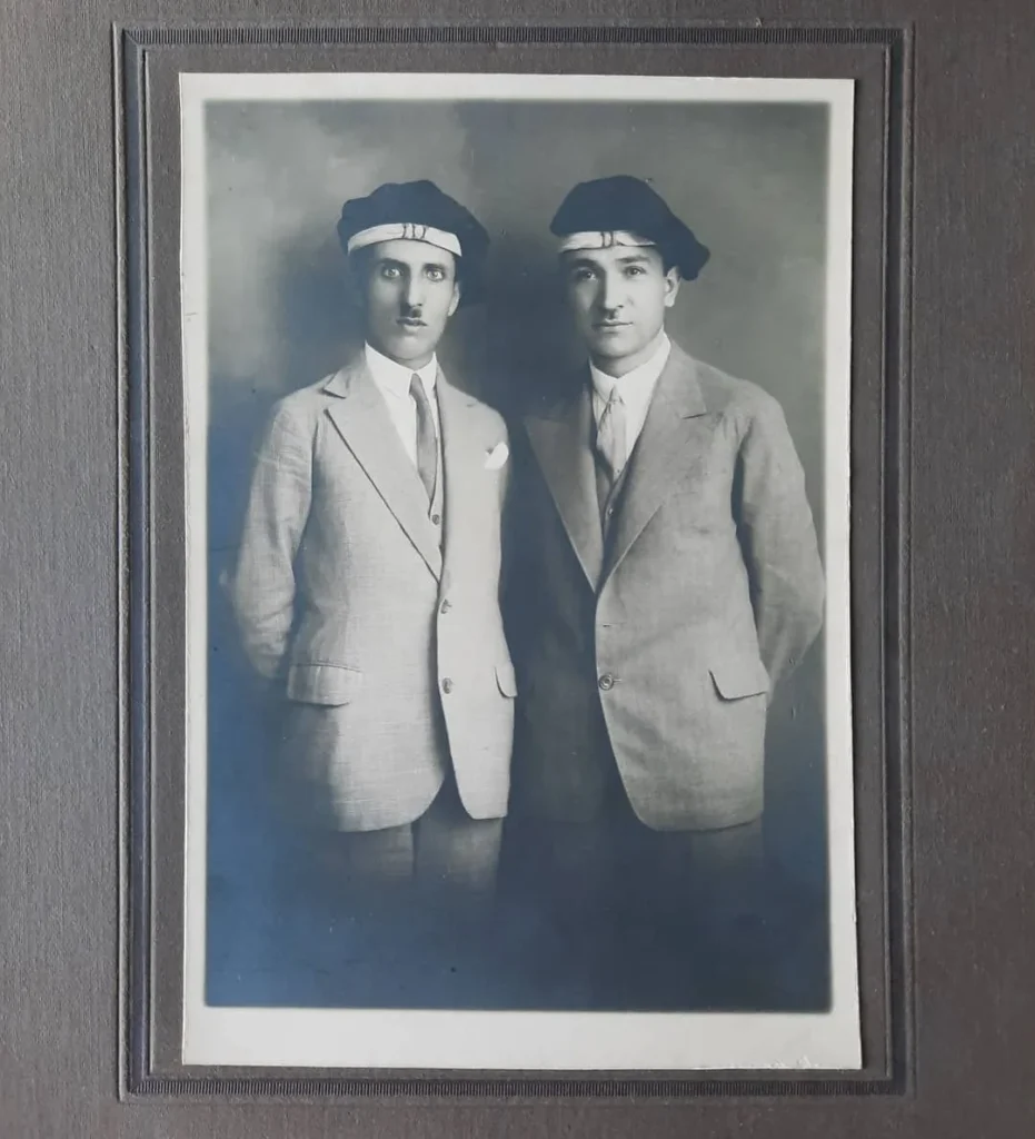 Başlarında şeritli bere, açık renk takım elbiseli iki gencin paspartulu stüdyo fotoğrafı