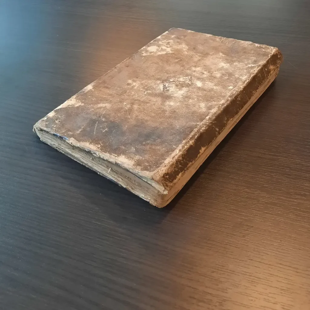 Kitabın yıpranmış deri cildi, masa üzerinde kapalı hâlde
