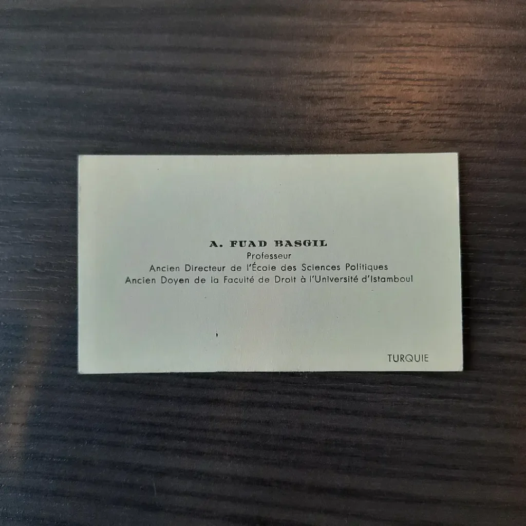 Ahşap zemin üzerinde 'A. Fuad Basgil' adını taşıyan Fransızca basılı kartvizit