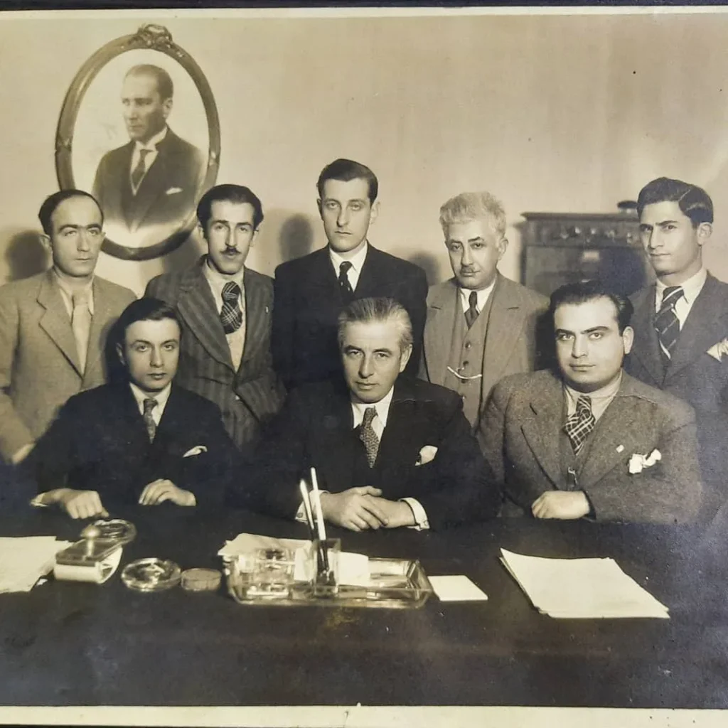 Duvarda Atatürk portresi bulunan makam odasında masa başında poz veren sekiz kişilik grup