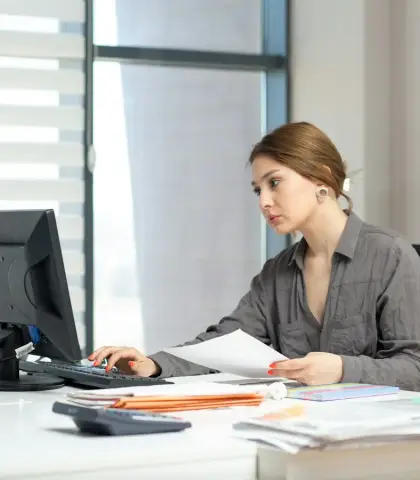 Ofis masasında bilgisayar ve belgelerle çalışan kadın