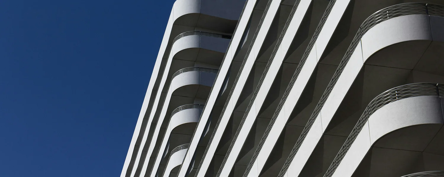 Modern residential building facade with white curved balconies against a navy-blue sky