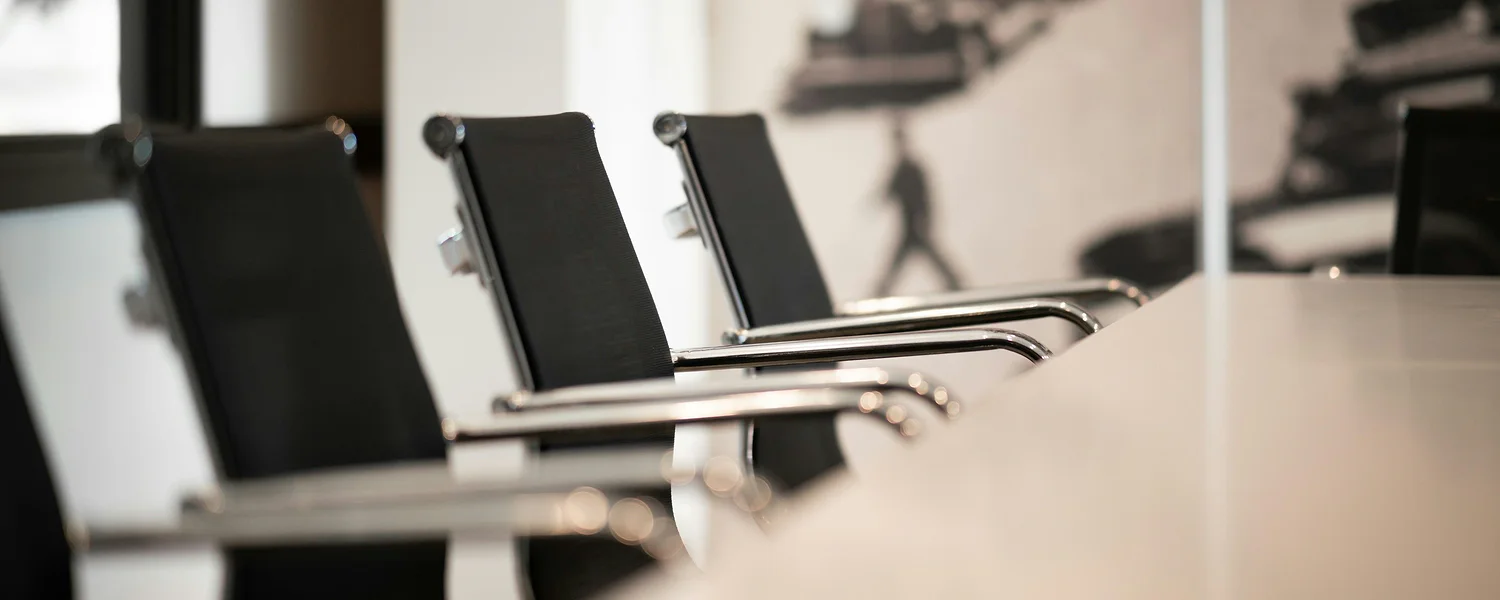 Black conference chairs with chrome armrests lined up along a white meeting table