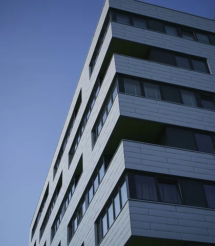 A multi-story residential building with a gray facade against a blue sky