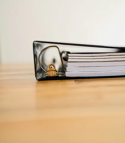 A black ring binder full of papers on a light wooden table