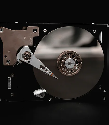Platter and read/write arm of a hard drive with its cover removed, on a black background