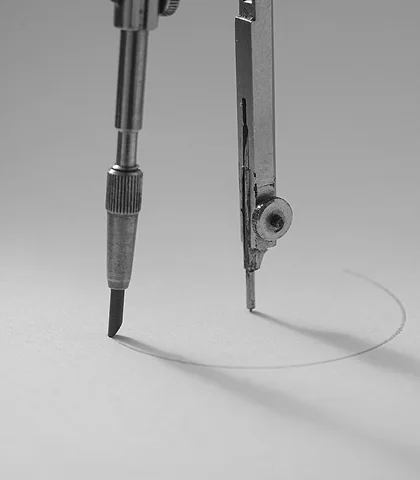Steel compass drawing a circle on gray paper