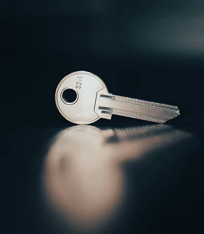 A single silver-colored key lying on a glossy navy-black surface