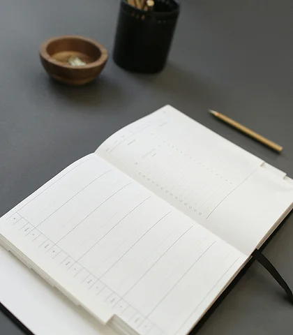 Open ruled accounting ledger and a brass pen on a gray table