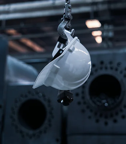 White hard hat hanging from a hook in a dark industrial plant