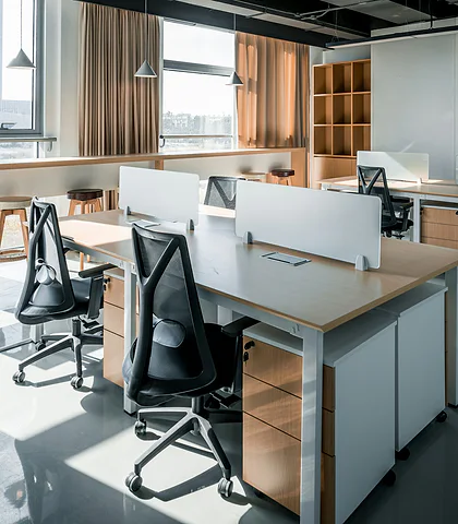 A bright office with desks separated by white partitions and black mesh chairs