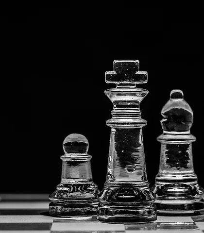 Glass chess king, pawn and bishop against a black backdrop
