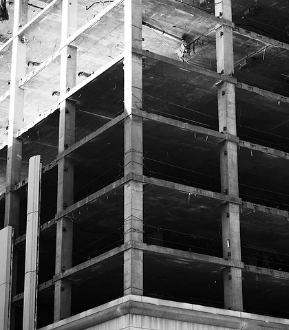 Black-and-white photo of a reinforced concrete building under construction, with its floors and columns visible